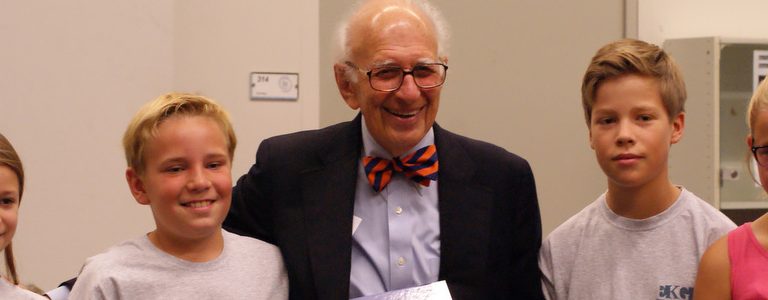 Ein Portraitfoto von dem Namensgeber der Schule, Eric Kandel. Er lacht und trägt eine Fliege - sein Markenzeichen.