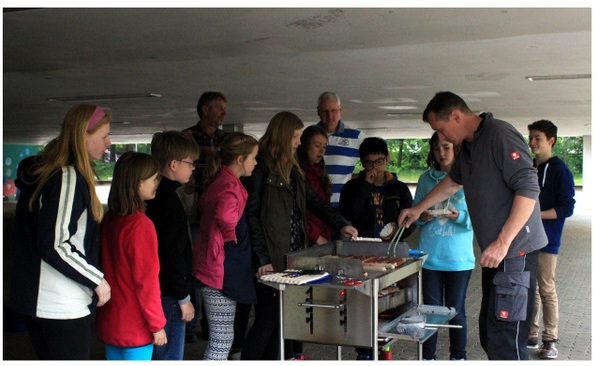 Grillen des Schulvereins. Mehrere Menschen stehen in einer Schlange vor dem Grill.