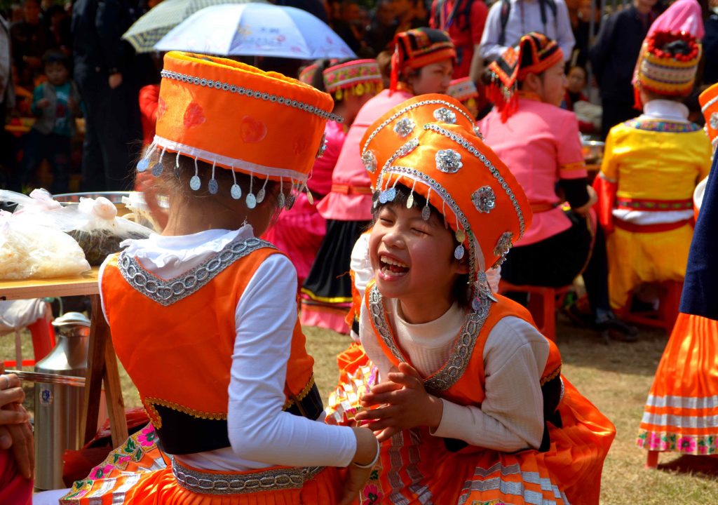 Ein lachendes Kind in orangenen, traditionallen Klamotten ist umgeben von anderen Personen
